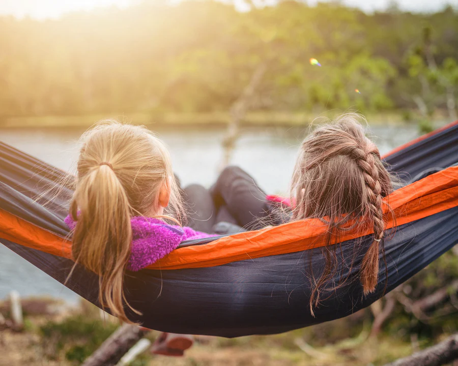 two girls from behind looking at a lake while lying in a hammock