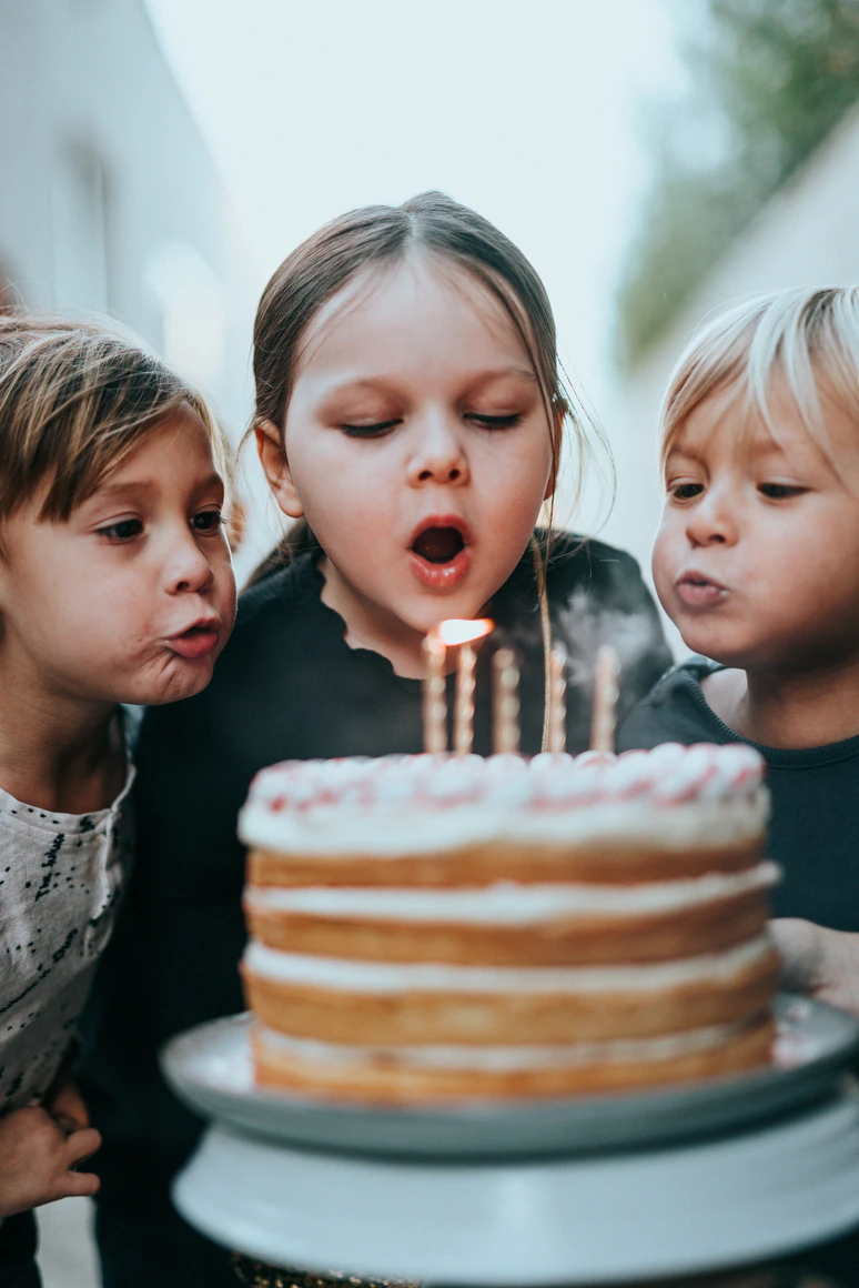 3 young kids blowing out candles on a cake